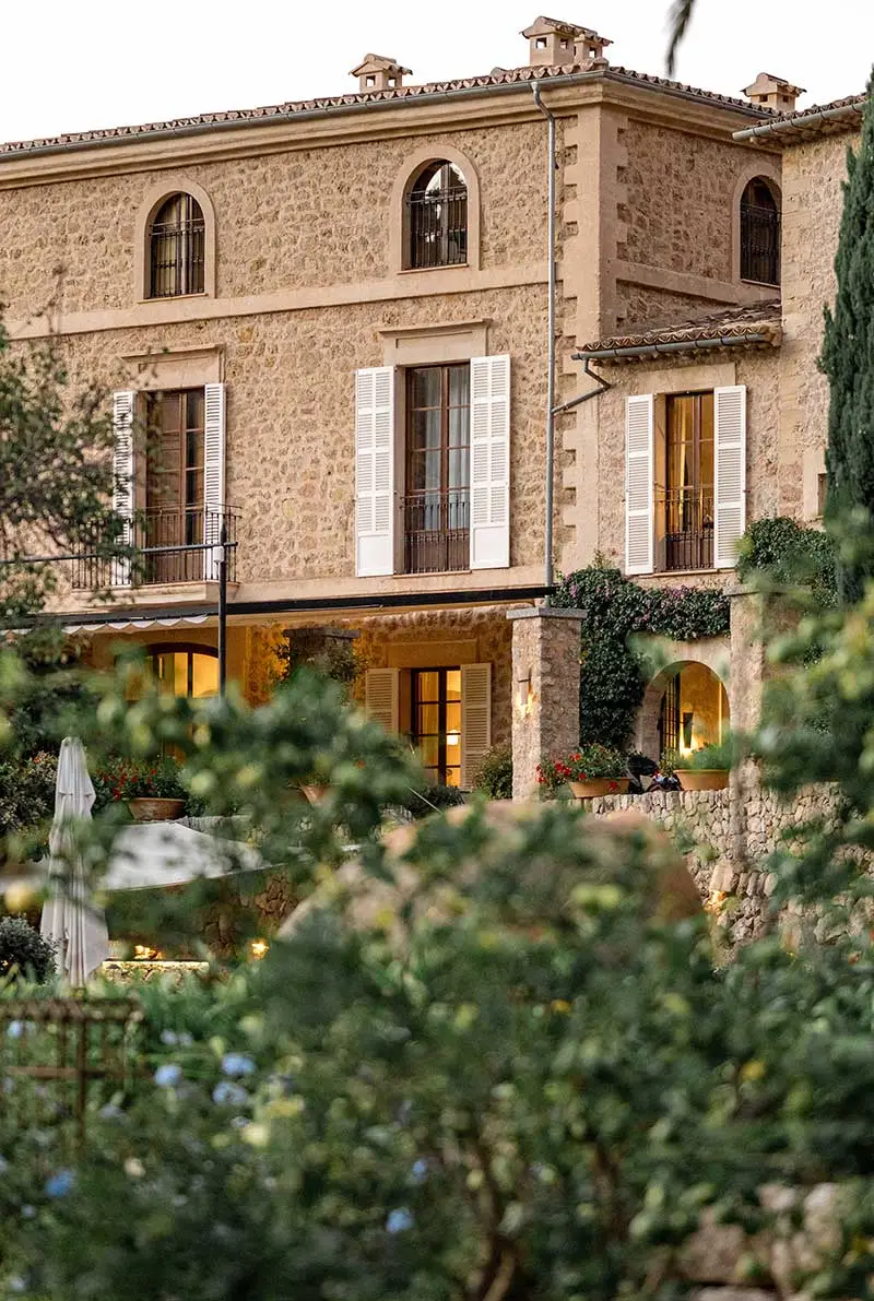 Exterior architectural view of the historic Belmond La Residencia hotel in Deià, Mallorca. The image showcases the traditional stone facade, white shutters, and lush Mediterranean gardens of this luxury wedding venue, captured by Knox Photographers